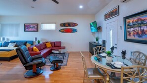 Una sala moderna con un sofá, una mesa de comedor preparada para cuatro personas y un ventilador de techo.
