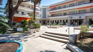 A multi-story hotel with a central courtyard, outdoor seating, and a large tree. - le corail by Interhome (Villeneuve-Loubet)