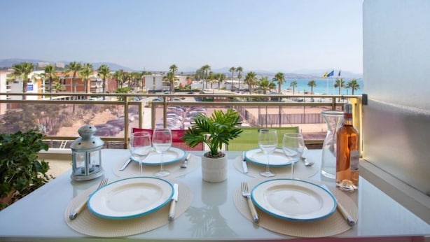 A balcony table set with plates, glasses, and a bottle, overlooking a beach and cityscape. - le corail by Interhome (Villeneuve-Loubet)
