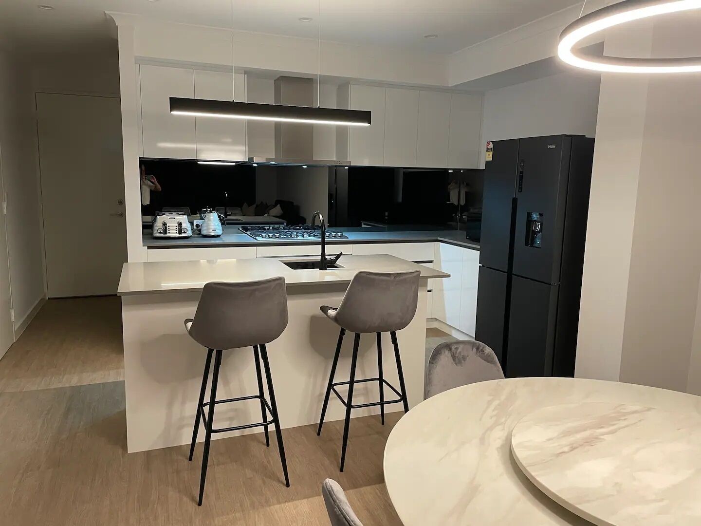 Een moderne keuken met witte kasten, een zwarte koelkast en twee barkrukken.