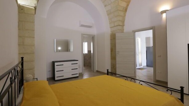 Un dormitorio con cama, cómoda, espejo y puerta que da a otra habitación.