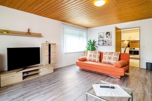 A modern living room with a flat-screen TV, orange sofa, and a glass coffee table.