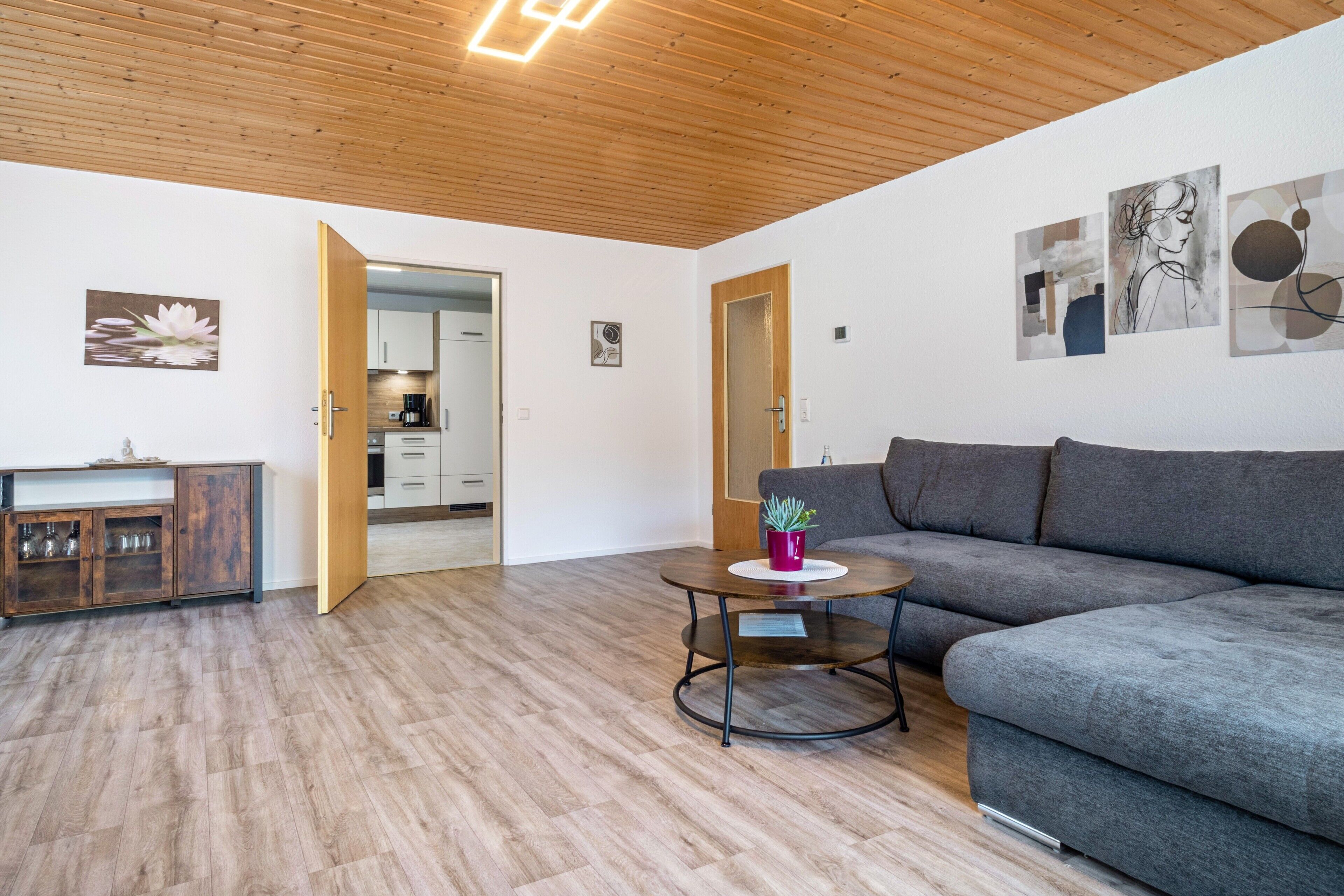 Una sala de estar moderna con un sofá gris, techo de madera y una pequeña mesa redonda con una planta en maceta.