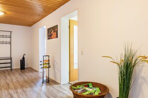 A hallway with wooden flooring, a wicker basket with magazines, a potted plant, and a door leading to another room.