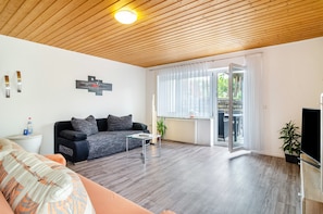 A modern living room with a sofa, a coffee table, a TV, and a sliding glass door leading to an outdoor area.