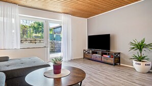 A modern living room with a sofa, round table, TV, and potted plants.