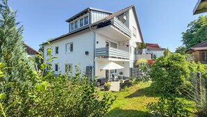 A two-story house with a balcony, a patio with outdoor furniture, and a garden area.
