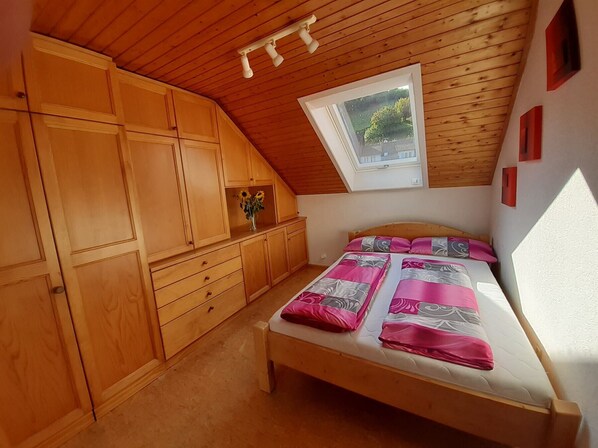 A bedroom with a sloped ceiling, wooden furniture, a skylight, and a bed with patterned bedding.