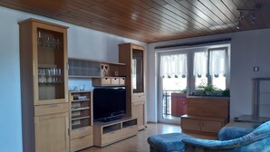 Un soggiorno con pavimento in legno, una televisione, armadietti e un divano blu.