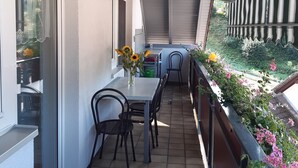 Un balcone con tavolo e sedie, un vaso con girasoli e vista sul verde.