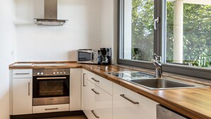 A kitchen with a Bosch oven, a coffee maker, a sink, and a window with a view of trees. - Apartment 'Am Lichtenberg' with Lake View, Private Terrace and Wi-Fi (Daisendorf)