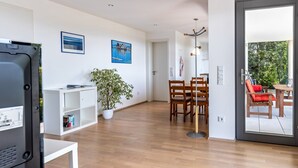A modern living room with a flat-screen TV, a white console table, a potted plant, and a dining area with wooden chairs and a red cushion. - Apartment 'Am Lichtenberg' with Lake View, Private Terrace and Wi-Fi (Daisendorf)