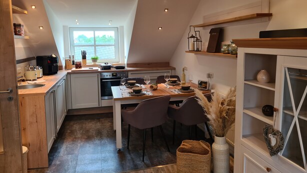 A modern kitchen with a dining area, wooden cabinetry, and a window providing natural light. - Apartment 'Rosenzauber Gipfelstürmer' with Shared Garden and Wi-Fi (Weißenstadt)