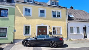 A two-story building with a green and yellow facade, a black car parked in front, and a small garden area. - Apartment 'Rosenzauber Gipfelstürmer' with Shared Garden and Wi-Fi (Weißenstadt)