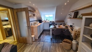 A modern kitchen with wooden cabinets, a dining table set for four, and a view of the outdoors through a window. - Apartment 'Rosenzauber Gipfelstürmer' with Shared Garden and Wi-Fi (Weißenstadt)