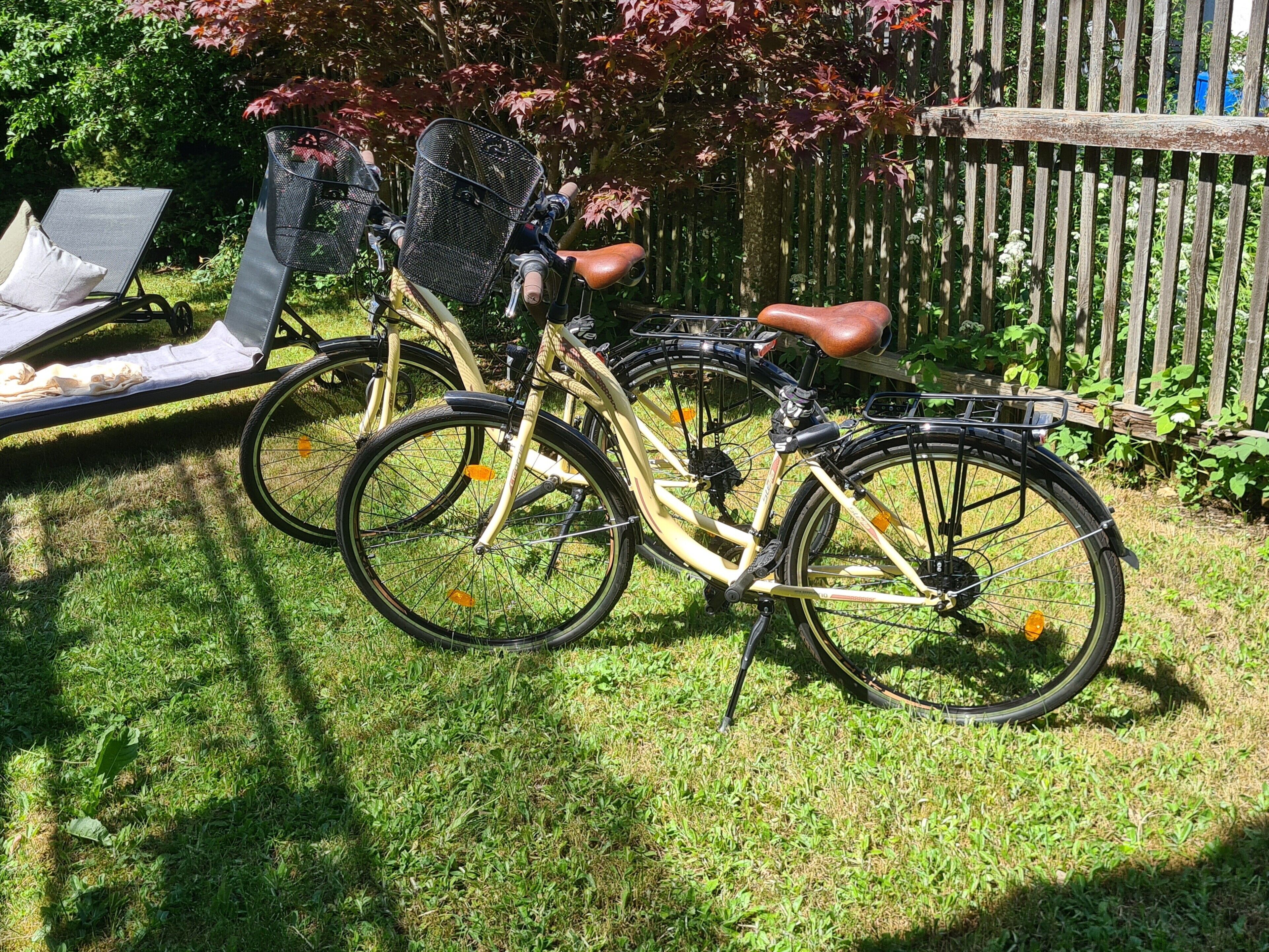 Una bicicleta estacionada sobre césped, con una cerca de madera y una silla al fondo.