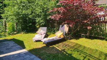 A backyard with two lounge chairs, a small tree with red leaves, and a wooden fence.