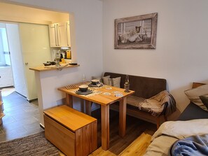 Um espaço compacto com cozinha compacta, mesa de jantar para dois, um banco e um sofá.