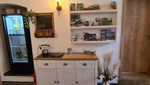 Una habitación con un armario de madera, un calendario en la pared, una estantería con libros y cajas, un refrigerador y un florero con plantas secas.