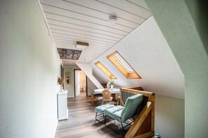 Et loftrum med træbjælker, ovenlysvinduer, et spiseområde og en siddekrog med en polstret bænk.