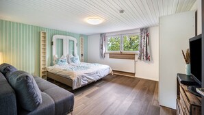 Un dormitorio con cama, sofá, televisor, ventana con cortinas y radiador.
