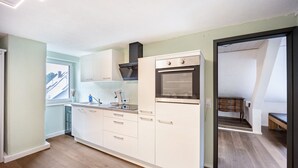 Una cocina compacta con armarios blancos, horno empotrado y ventana.