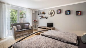 Une pièce comprenant un canapé, un téléviseur, un lit et une fenêtre avec des rideaux.