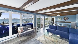 A spacious living area with a view of the water, featuring a blue sofa, a glass coffee table, and a wooden ceiling. - ⚓️Direct lake Lakefront Home Tritoon rental available (Syracuse)