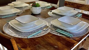 A dining area with a wooden table set for four, surrounded by white cabinets and a microwave.