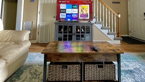 A living room with a television on a wooden coffee table, a beige couch, and a staircase.