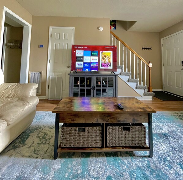 A living room with a television on a wooden coffee table, a beige couch, and a staircase.