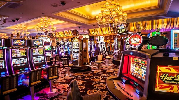 A casino with multiple slot machines, a chandelier, and a carpeted floor.