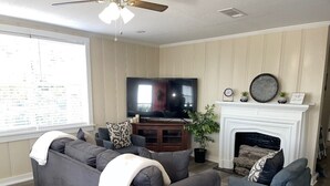 Ein Wohnzimmer mit großem Flachbildfernseher, Kamin und einer Sofagarnitur.