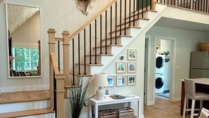 Un vaste espace de vie agrémenté d’un escalier en bois, d’une peau d’animal décorative accrochée au mur, d’une plante en pot et d’une table basse avec une télécommande.