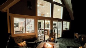 Un espace extérieur accueillant avec un foyer, une terrasse en bois et de grandes fenêtres donnant sur une cuisine et un espace de vie.