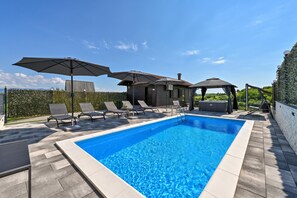 Una piscina rectangular con una terraza empavedada, rodeada de sillas de descanso y sombrillas.