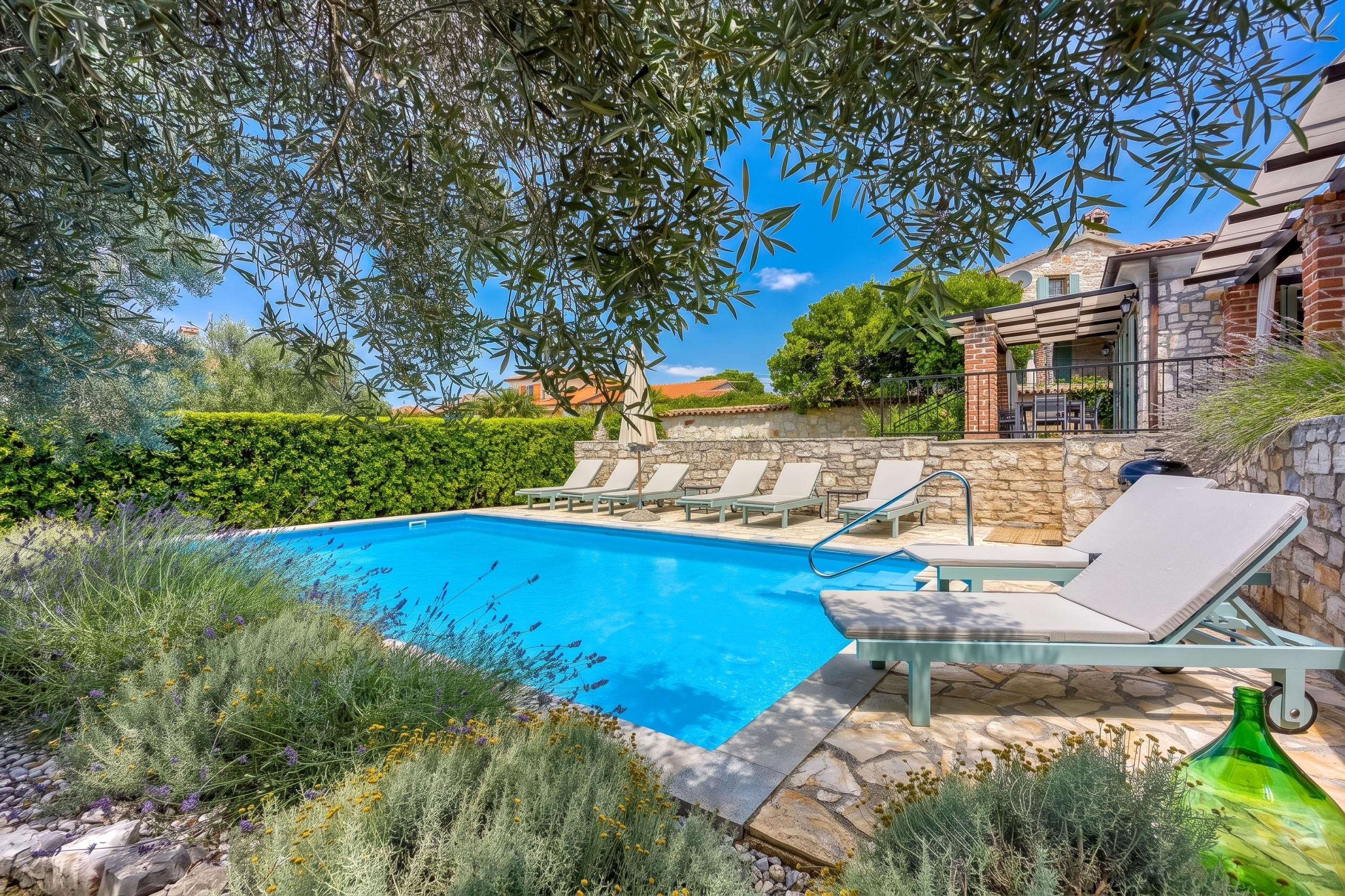 A swimming pool with lounge chairs, surrounded by greenery and stone walls.