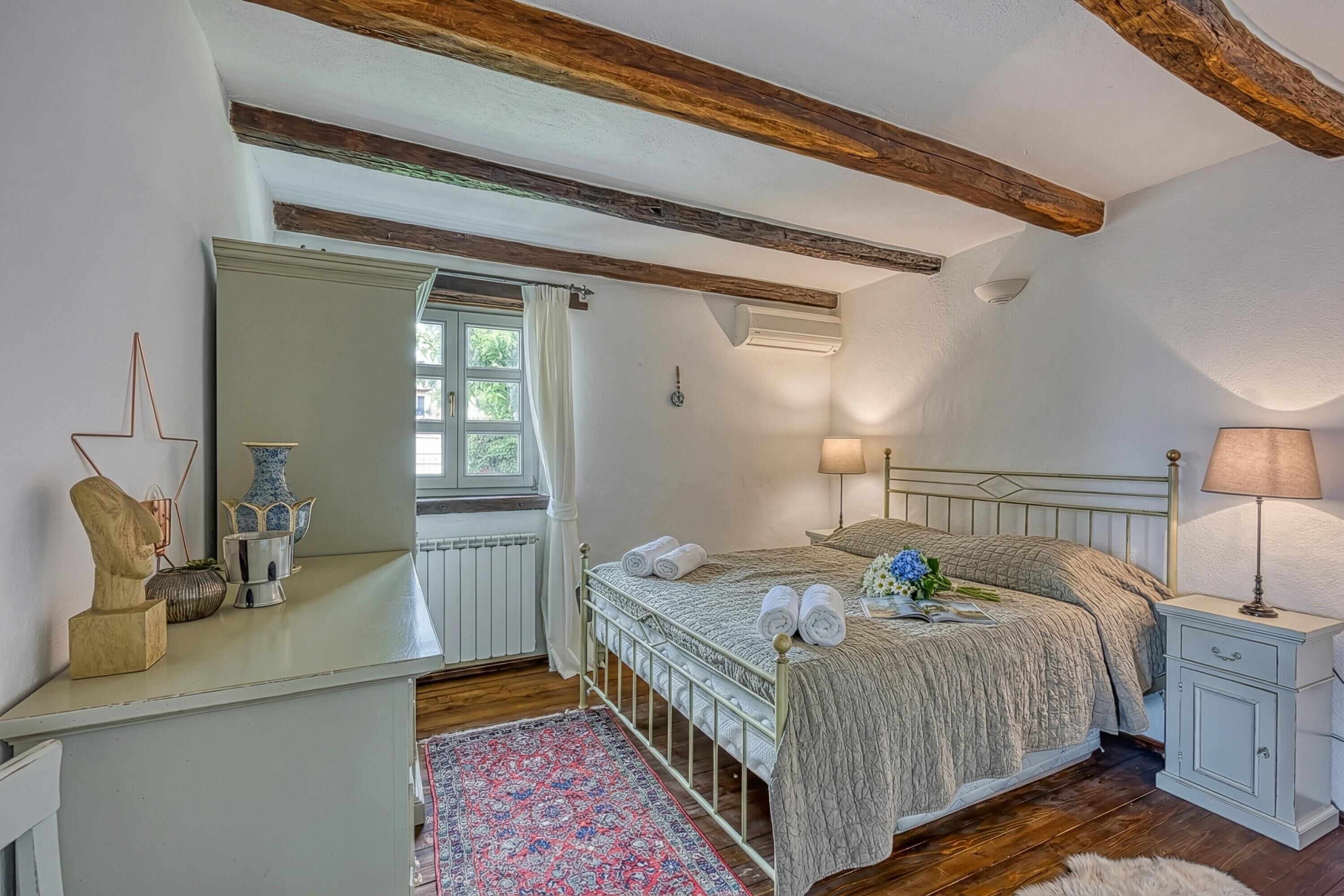 A bedroom with a bed, bedside tables, a mirror, a window, and a radiator.