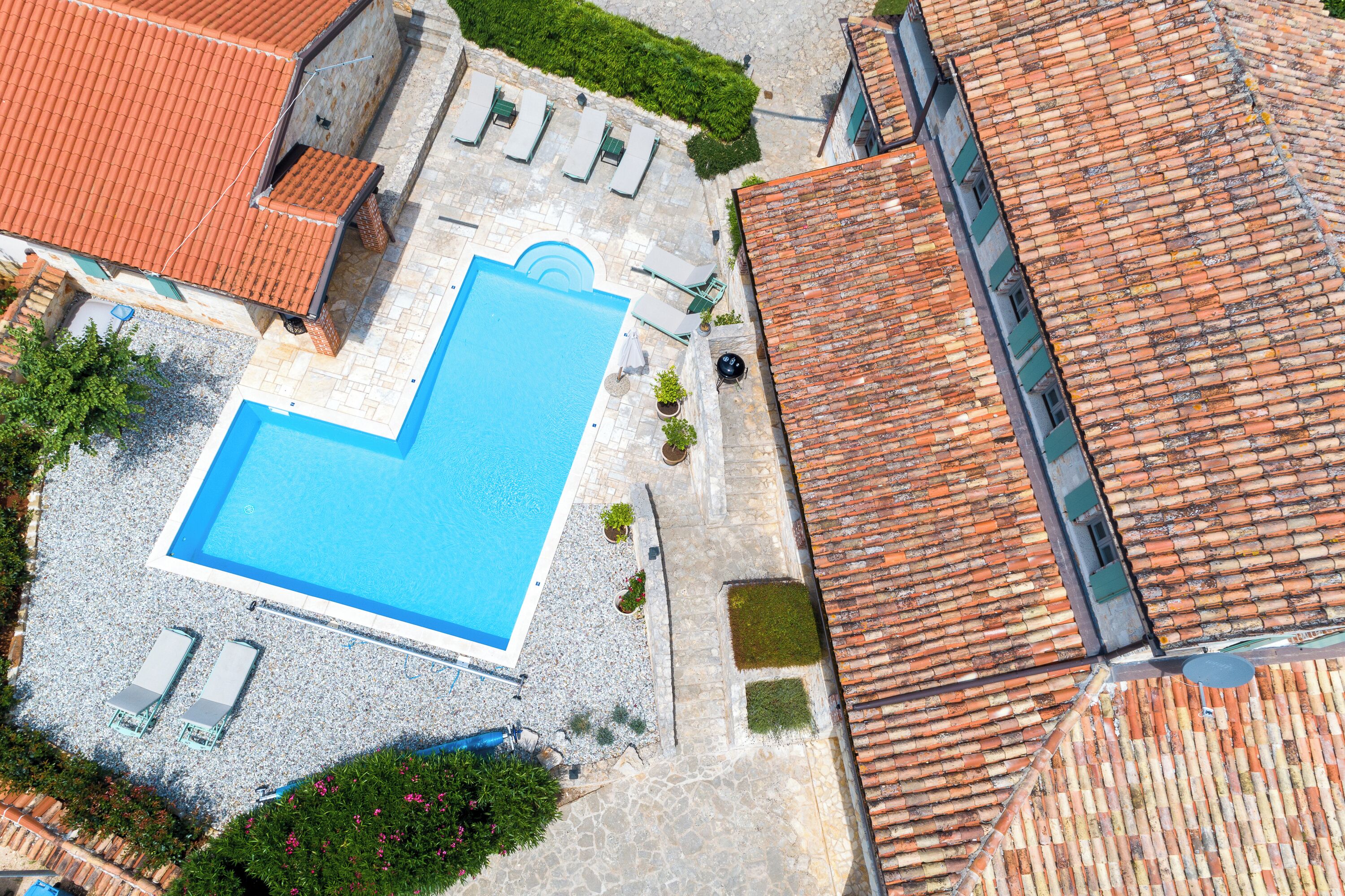 An aerial view of a property with a swimming pool, lounge chairs, and a tiled roof.