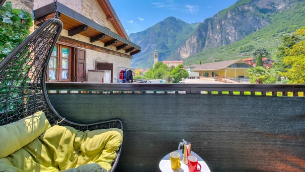 A balcony with a hanging chair, a small table with a coffee pot and cups, and a mountain view.