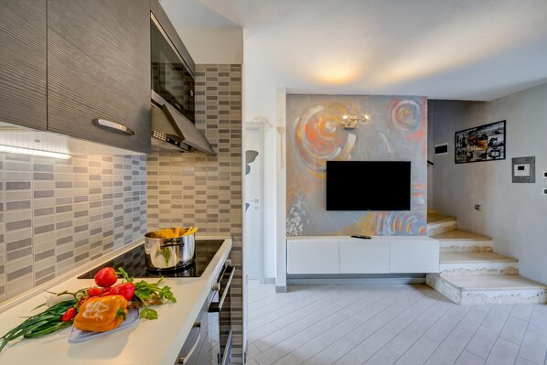A modern kitchen with a tiled backsplash, a flat-screen TV mounted on a wall, and a staircase leading to an upper level.