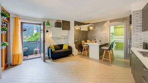 A modern interior with a sofa, dining area, kitchen, and a view of a building through a door.
