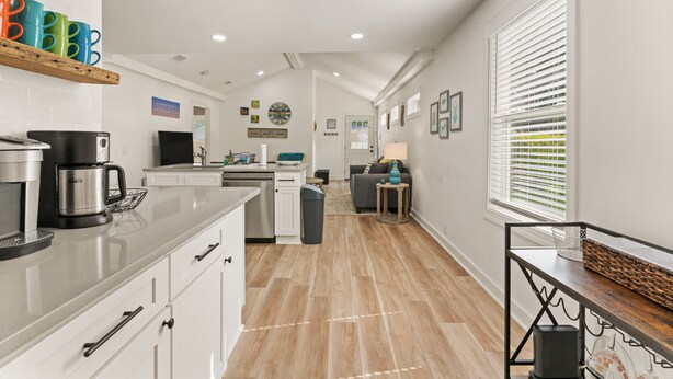 A modern kitchen with white cabinets, a coffee maker, and a dining area with a table and chairs. - Sunflower Hideaway -Walk to eats, bike to beach, pet friendly, Relaxed backyard. (St. Simons Island)
