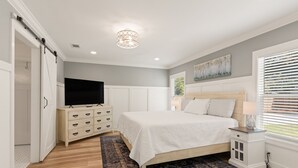 A bedroom with a bed, a dresser, a TV, and a window with blinds. - Sunflower Hideaway -Walk to eats, bike to beach, pet friendly, Relaxed backyard. (St. Simons Island)