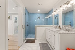 A modern bathroom with a walk-in shower, dual sinks, and a large mirror. - Sunflower Hideaway -Walk to eats, bike to beach, pet friendly, Relaxed backyard. (St. Simons Island)