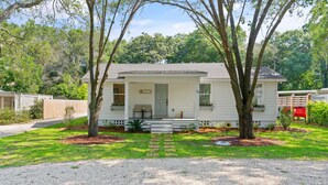 A single-story house with a front porch, a small front yard, and a gravel driveway. - Sunflower Hideaway -Walk to eats, bike to beach, pet friendly, Relaxed backyard. (St. Simons Island)