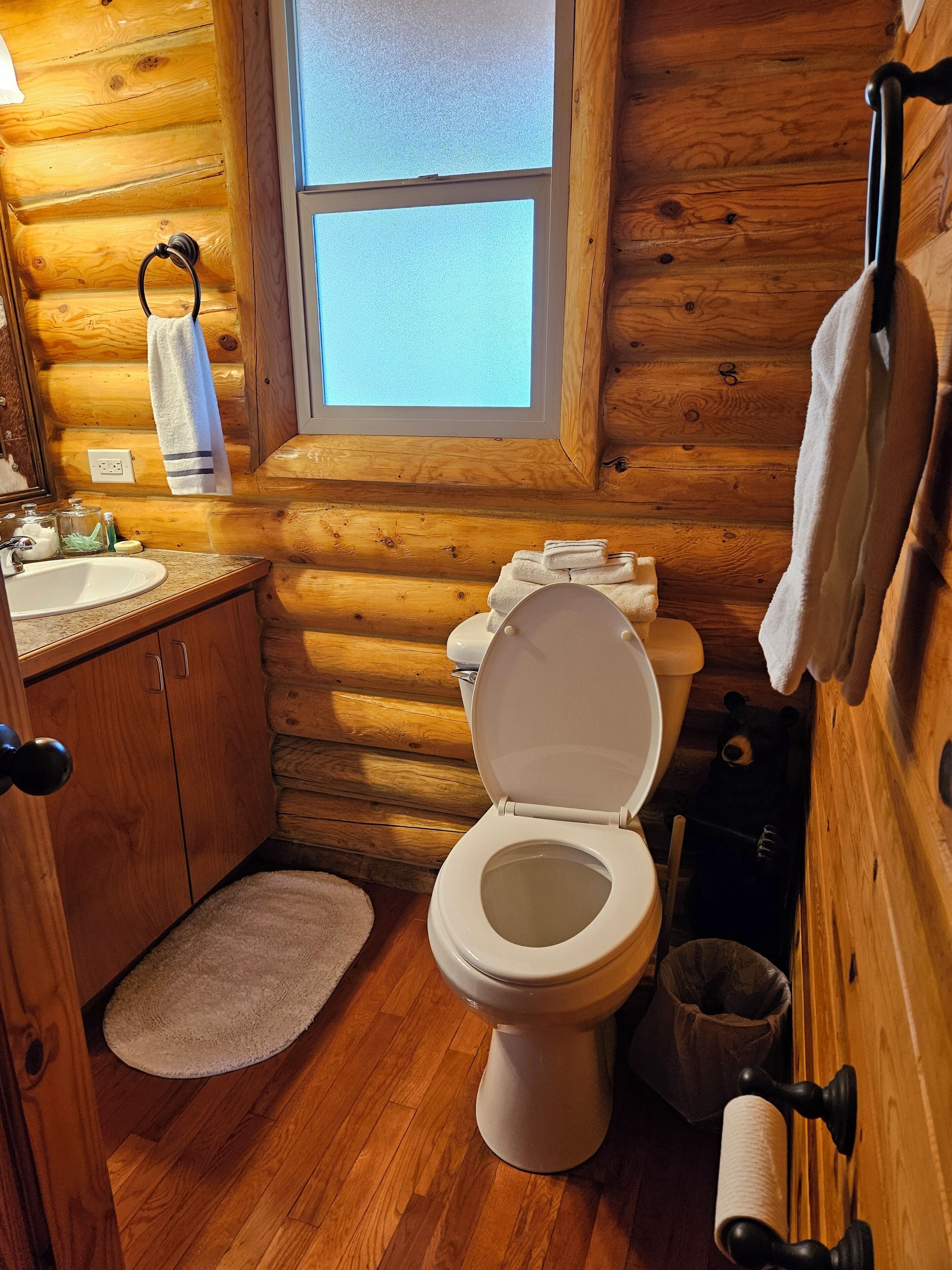 A wooden cabin bathroom with a toilet, sink, and window.