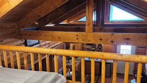 L’intérieur d’un chalet en bois, avec une chambre à coucher située en mezzanine, une rambarde en bois et une vue sur l’espace intérieur à travers une fenêtre.