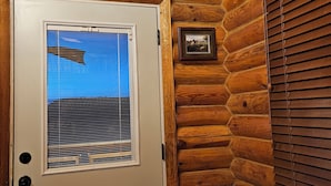 Une cabane en bois avec une porte blanche, une fenêtre avec des stores et un tableau encadré accroché au mur.