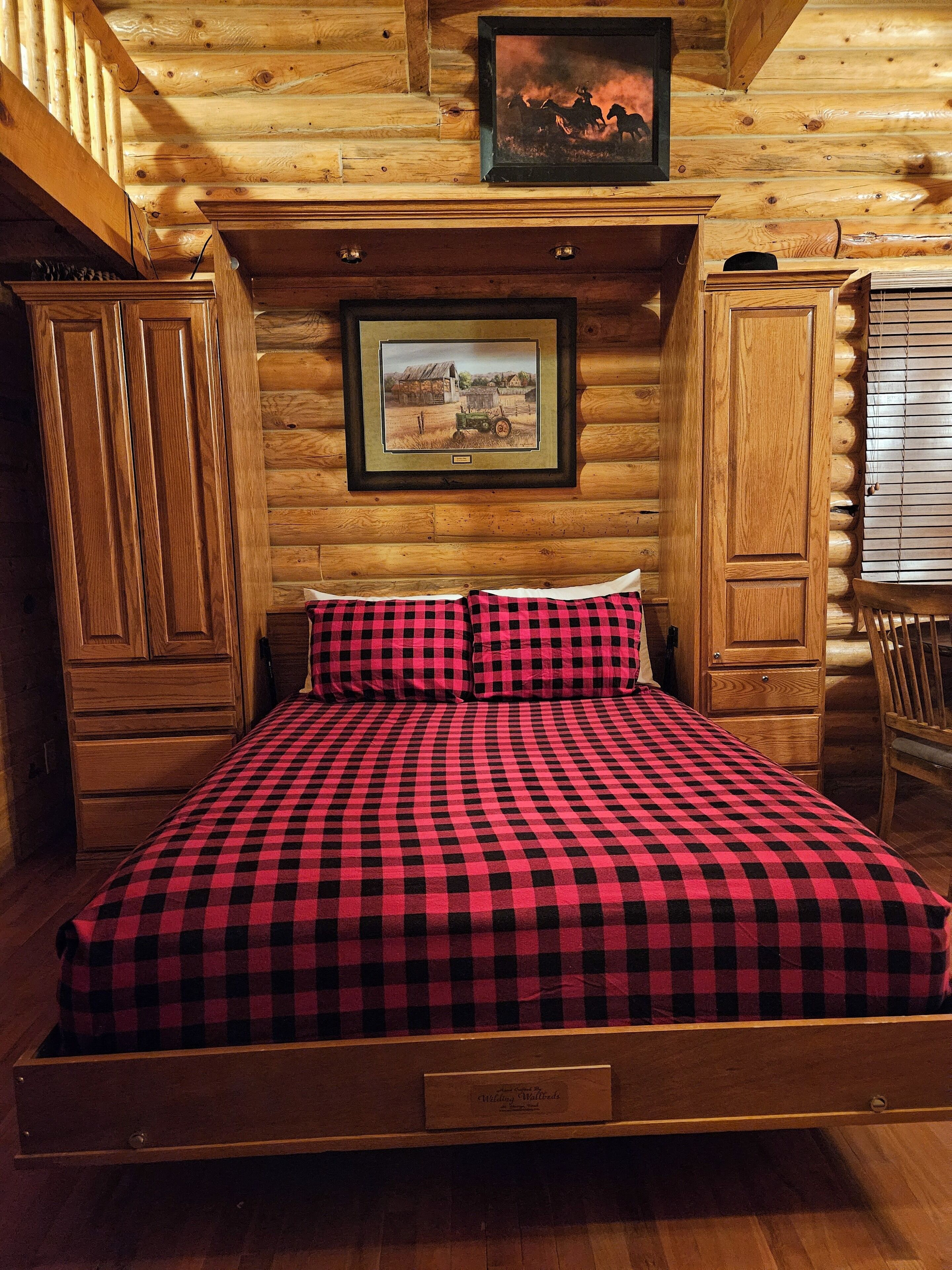 Een slaapkamer in een houten blokhut, met een bed, twee houten kasten en een lijst met een foto aan de muur.